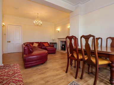 A living room with a red leather sofa wooden dining table and chairs and a fireplace at Fir Grove in Menai Bridge