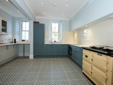 A kitchen with blue and beige cabinets tiled floor and windows at Fir Grove in Menai Bridge
