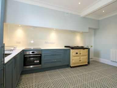 A kitchen with blue cabinets white countertops patterned floor and an oven at Fir Grove in Menai Bridge