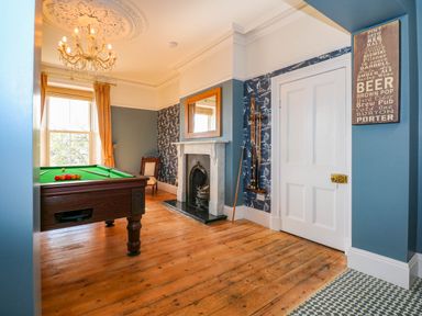 A game room with a pool table wooden floor fireplace and a window with curtains at Fir Grove in Menai Bridge