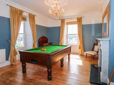 A room with a billiard table wooden floors large windows and a chandelier at Fir Grove in Menai Bridge