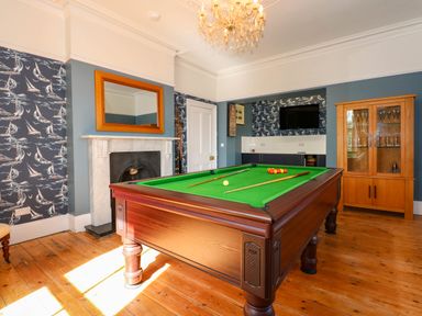 A billiard room with a pool table a wooden cabinet a fireplace and a wall-mounted TV at Fir Grove in Menai Bridge