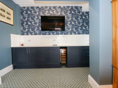 A kitchen area with navy blue cabinets a wine cooler a flat screen TV and sailboat wallpaper at Fir Grove Menai Bridge