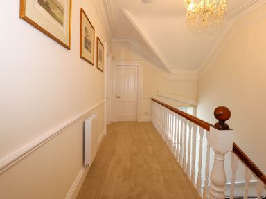 A hallway with framed pictures on the wall a chandelier and a wooden railing at Fir Grove in Menai Bridge
