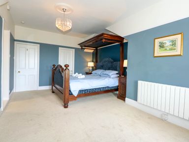 A bedroom with a wooden canopy bed blue walls two white doors and a framed picture at Fir Grove Menai Bridge