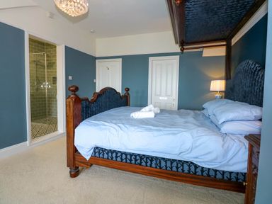 A bedroom with a wooden bed a blue upholstered headboard a bedside table with a lamp and an open door revealing a bathroom at Fir Grove in Menai Bridge