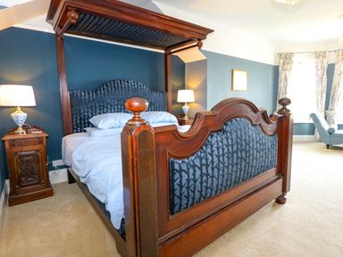 A bedroom with a wooden four-poster bed two bedside tables with lamps and a chaise lounge at Fir Grove in Menai Bridge
