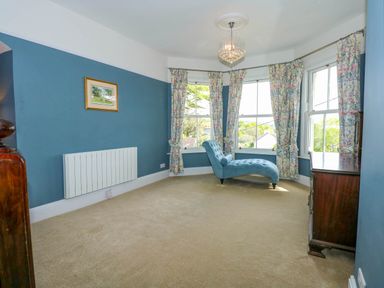 A room with blue walls a chaise lounge floral curtains and wooden furniture at Fir Grove in Menai Bridge