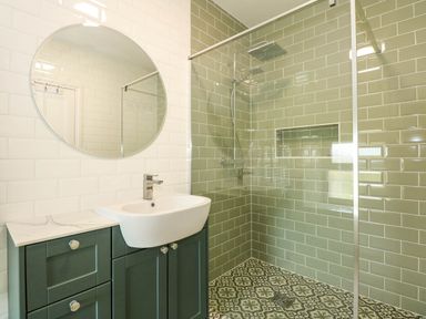 A bathroom with a sink and mirror and a walk in shower with green wall tiles and patterned floor tiles at Fir Grove in Menai Bridge