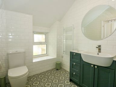 A bathroom with patterned floor tiles a toilet a sink with green cabinets and a round mirror at Fir Grove in Menai Bridge