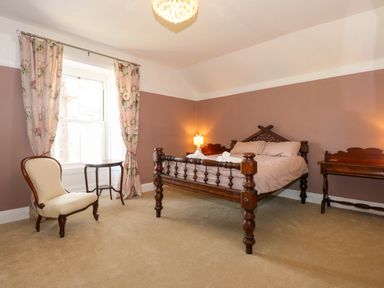 A bedroom with a wooden bed two bedside tables a chair and floral curtains at Fir Grove in Menai Bridge