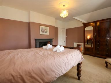 A bedroom with a bed, rolled towels on the bed, a wooden wardrobe with a mirror, and a fireplace at Fir Grove in Menai Bridge