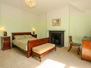 A bedroom with a wooden bed two bedside tables a cushioned bench a chair a dresser and a fireplace at Fir Grove in Menai Bridge