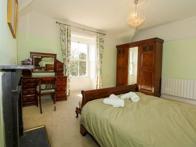 A bedroom with a wooden bed green bedding an antique wooden dresser with a mirror a wooden wardrobe and floral curtains at Fir Grove in Menai Bridge