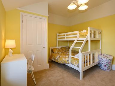 A bedroom with a white bunk bed yellow walls a white desk a chair and a lamp at Fir Grove in Menai Bridge