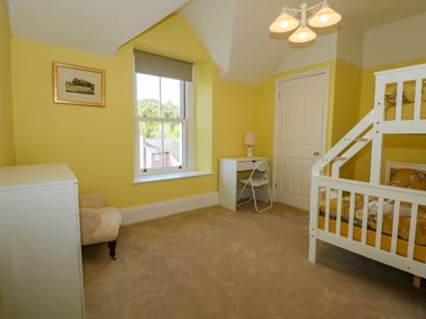 A bedroom with bunk beds a desk with chair and lamp a chest of drawers and an armchair at Fir Grove in Menai Bridge