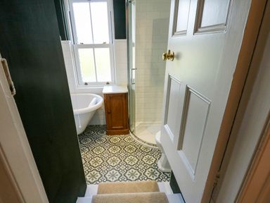 A bathroom with patterned floor tiles a wooden cabinet a clawfoot bathtub and a glass shower enclosure at Fir Grove in Menai Bridge