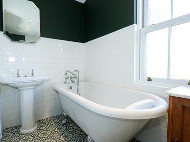 A bathroom with a clawfoot bathtub a pedestal sink patterned floor tiles and a window at Fir Grove in Menai Bridge
