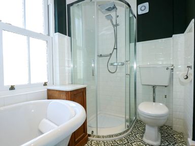A bathroom with a corner shower, toilet, bathtub, wooden cabinet, white tiles, patterned floor at Fir Grove in Menai Bridge