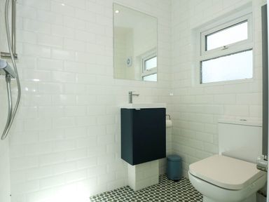 A bathroom with a toilet a sink with a cabinet a mirror a window and a showerhead at Fir Grove in Menai Bridge