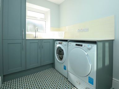 A laundry room with washing machine dryer under a counter and blue cabinets at Fir Grove Menai Bridge