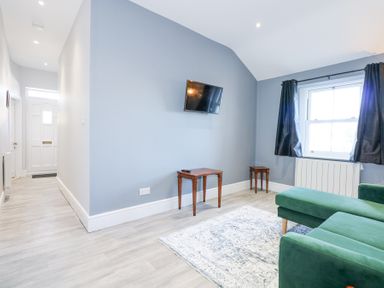 A living room with green sofa a rug a wall-mounted TV two wooden tables and a window with black curtains at The Fir Grove Annex in Menai Bridge