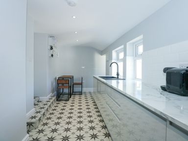 A kitchen with patterned floor tiles wooden chairs and table and a marble countertop with a black toaster at The Fir Grove Annex in Menai Bridge