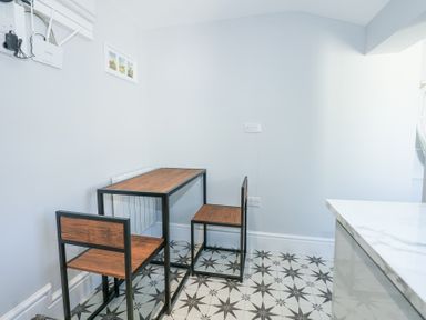 A small dining area with a wooden table and two chairs on patterned floor tiles at The Fir Grove Annex in Menai Bridge