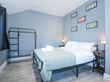 A bedroom with a metal bed frame two bedside tables with lamps a metal clothes rack and framed pictures on a blue wall at The Fir Grove Annex in Menai Bridge