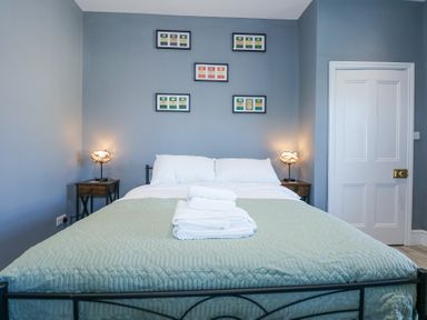 A bedroom with a bed and folded towels on it two bedside tables with lamps and framed pictures on the wall at The Fir Grove Annex in Menai Bridge