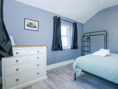 A bedroom with a white chest of drawers a bed with folded towels black curtains and a metal clothes rack at The Fir Grove Annex in Menai Bridge