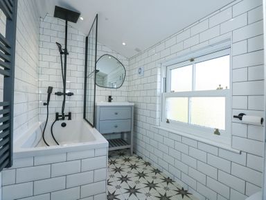 A bathroom with a bathtub shower combination a vanity with a mirror and a window at The Fir Grove Annex in Menai Bridge