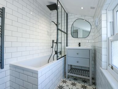 A bathroom with a bathtub with a shower, a gray vanity with a mirror above it, and patterned floor tiles at The Fir Grove Annex in Menai Bridge
