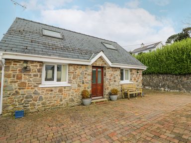 A stone house with a wooden door two windows a bench and potted plants on a paved driveway at Trevone in Goodwick