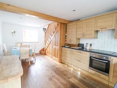 A kitchen with wooden cabinets and a dining table near a staircase at Trevone in Goodwick