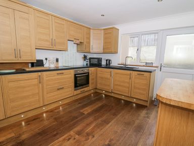A kitchen with wooden cabinets black countertops and wooden floor at Trevone in Goodwick