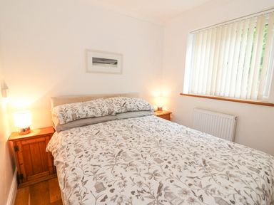A bedroom with a double bed between two wooden bedside tables with lamps and a window with vertical blinds at Trevone in Goodwick