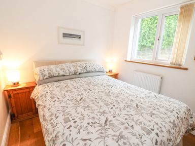 A bedroom with a double bed patterned duvet two wooden bedside tables with lamps and a window at Trevone in Goodwick