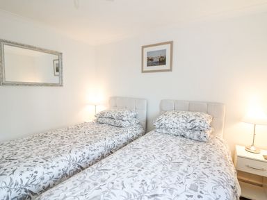 A bedroom with two single beds with floral bedding a nightstand with lamp a mirror on the wall and a framed picture at Trevone in Goodwick
