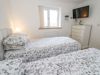 A bedroom with two single beds with patterned bedding a dresser a wall mounted TV and a window at Trevone in Goodwick