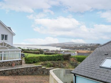 A view of coastal houses with hedges green lawns and hills in the background at Trevone in Goodwick