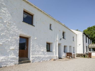 White stone building with multiple windows and doors and a wooden bench outside at Bramble Cottage in Thornthwaite near Braithwaite