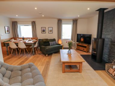 A living room with a sofa, dining table, and television at Bramble Cottage in Thornthwaite near Braithwaite