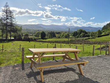 A picnic table on gravel with mountains in the background at Bramble Cottage Thornthwaite near Braithwaite