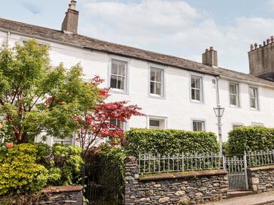 Row of white terraced houses with chimneys in front of stone wall and green hedges at Middletown in Keswick