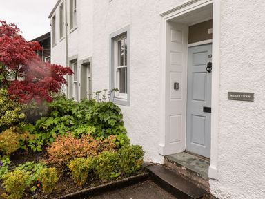 An exterior view of a white house with a blue door and various plants including a red-leaved tree at Middletown in Keswick