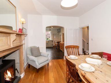 A dining room with a wooden table set with plates and glasses a light blue armchair a fireplace and an archway leading to a kitchen at Middletown in Keswick