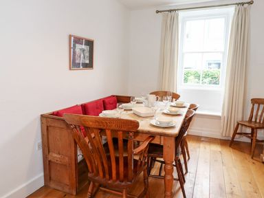 A dining room with wooden table and chairs set with dishes and glasses near a window with cream curtains at Middletown in Keswick