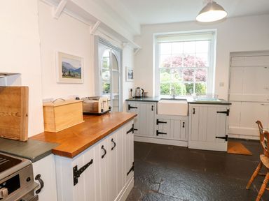 A kitchen with wooden countertop cabinets a toaster kettle a sink and a window showing trees at Middletown in Keswick
