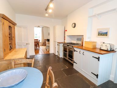 A kitchen with wooden cabinets, a stove, a refrigerator, a blue table with chairs, and a wooden cupboard at Middletown in Keswick